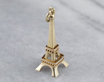 May include: A gold-colored Eiffel Tower charm pendant. The charm is detailed with small arches and a rounded top.