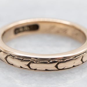 May include: A gold wedding band with a textured, patterned design. The band is thin and has a smooth, polished finish.