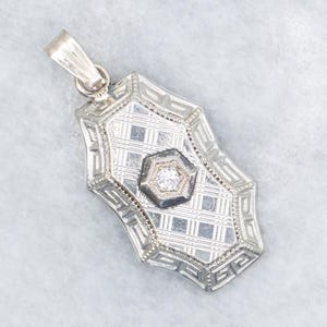 May include: A silver pendant with an Art Deco design. The pendant has a rectangular shape with a geometric pattern and a central hexagon with a small, round, clear stone. The bail is a simple loop.