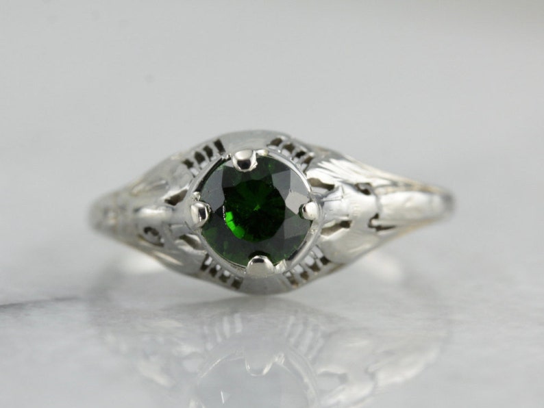 May include: A silver ring with a delicate filigree design and a round green gemstone.