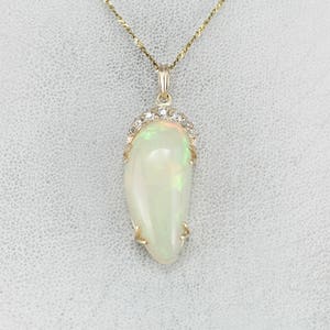 May include: A gold chain necklace with a pendant featuring a white opal stone surrounded by a halo of small diamonds.
