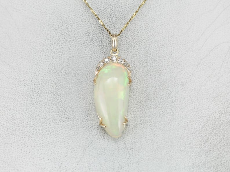May include: A gold chain necklace with a pendant featuring a white opal stone surrounded by a halo of small diamonds.
