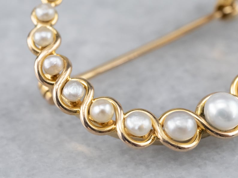 Puede incluir: Un broche de oro con un delicado dise&ntilde;o de perlas blancas dispuestas en espiral.
