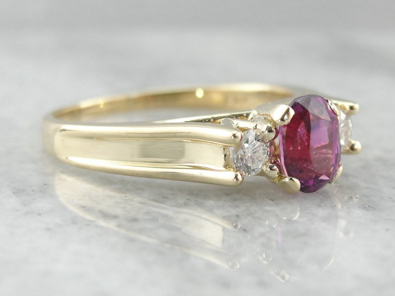 May include: A gold ring with a large oval ruby gemstone and two smaller round diamonds on either side.