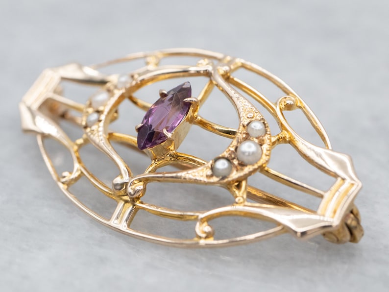 May include: A gold-toned brooch with a delicate, intricate design featuring a purple gemstone and pearl accents.