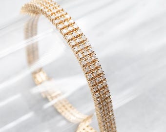 May include: A gold bracelet with three rows of small, clear diamonds.