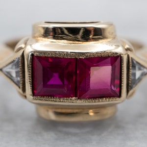 May include: A gold ring with two square-shaped ruby stones and two triangular-shaped diamond stones.