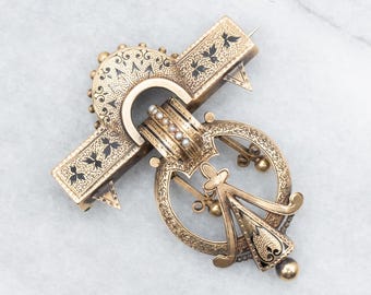 May include: A gold-tone brooch with black enamel detailing and pearl accents. The brooch features a geometric design with a central oval shape and a cross-shaped element.