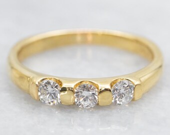 May include: A gold band ring with three round diamonds set in a row.