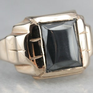 May include: A gold ring with a black square-shaped gemstone set in a textured band.