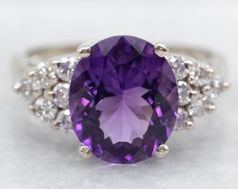 May include: A silver ring featuring a large oval amethyst gemstone surrounded by smaller diamonds.