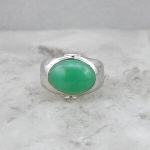 May include: A silver ring with a green oval gemstone set in the center. The ring has a textured band.