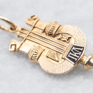 Pode incluir: Charme de pingente dourado com um design detalhado que apresenta uma lira, uma bússola e uma esquadria, e as letras "I.M.I." em esmalte preto. O charme tem um laço para prender a uma corrente ou pulseira.