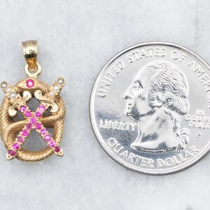 May include: Gold pendant with a design of two crossed swords surrounded by a snake, all set with pink and white stones.