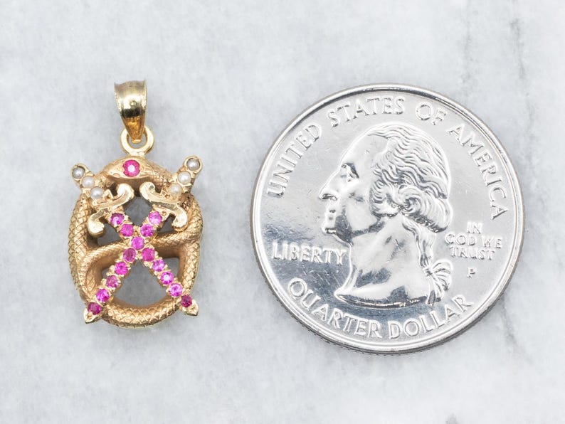 May include: Gold pendant with a design of two crossed swords surrounded by a snake, all set with pink and white stones.