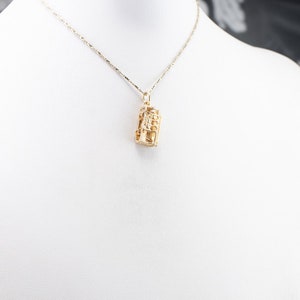 May include: A gold chain necklace with a gold pendant shaped like a small building. The pendant has a detailed design and is hanging from a delicate chain.