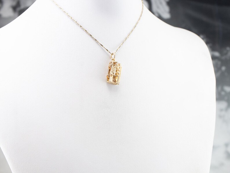 May include: A gold chain necklace with a gold pendant shaped like a small building. The pendant has a detailed design and is hanging from a delicate chain.