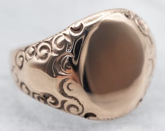Puede incluir: Un anillo de sello de oro con una parte superior ovalada lisa y un diseño decorativo en espiral alrededor de la banda.