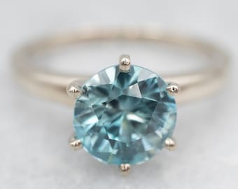 May include: A delicate gold ring with a large, round, light blue gemstone set in a six-prong setting.