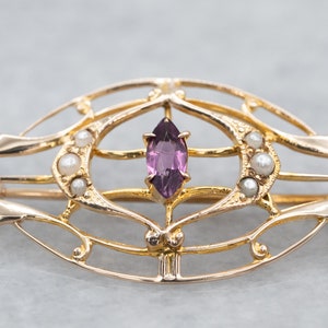May include: A gold-toned brooch with a delicate, openwork design featuring a purple gemstone and small pearls.