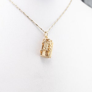 May include: A gold chain necklace with a pendant shaped like a small, rectangular box with a detailed design. The box has a small, clear stone in the center.