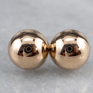 May include: A pair of round, gold-toned earrings. The earrings are smooth and shiny.
