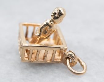 Op de afbeelding: Gouden bedel van een baby in een wieg. De bedel is gedetailleerd en heeft een lus om aan een ketting of armband te bevestigen.