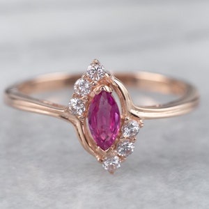 May include: A rose gold ring with a marquise-shaped ruby gemstone surrounded by smaller white gemstones.