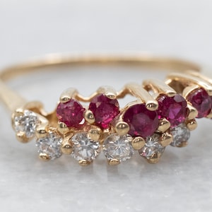 May include: A gold ring with a row of red rubies and diamonds set in a curved design.