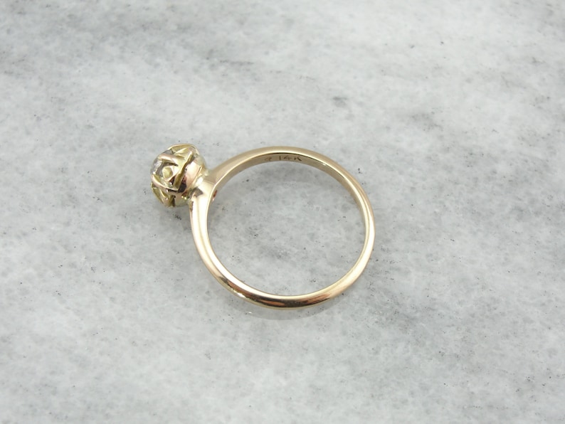 Puede incluir: Un anillo de oro con un solo diamante redondo engastado en un engaste de bisel. El anillo est&aacute; marcado con "15K" en el interior de la banda.
