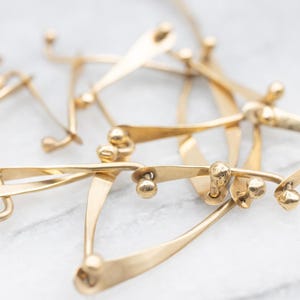May include: Close-up of a gold-toned necklace with an abstract design. The necklace features multiple interconnected, curved elements with small, spherical accents. The metal has a polished finish, and the piece is set against a light background.