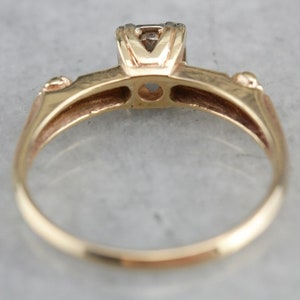 May include: A gold ring with a single diamond set in a prong setting. The ring has a simple band and a smooth finish.