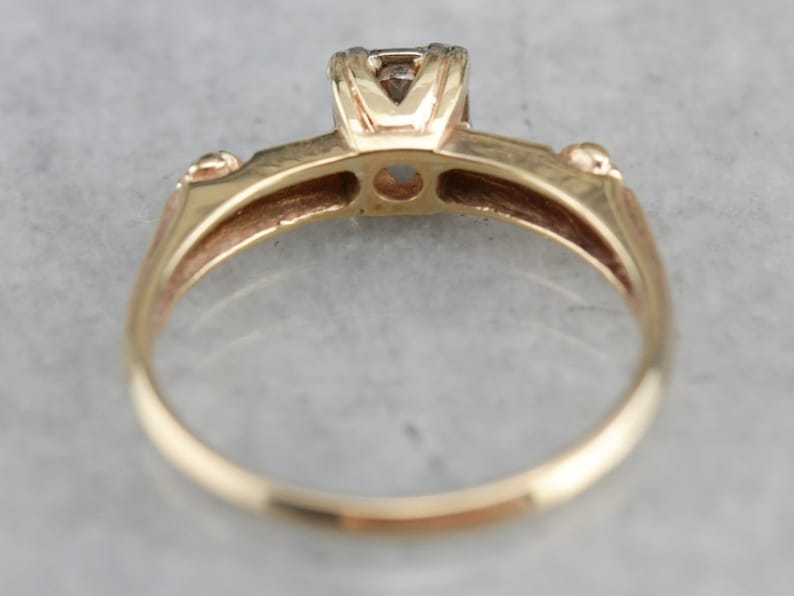 May include: A gold ring with a single diamond set in a prong setting. The ring has a simple band and a smooth finish.