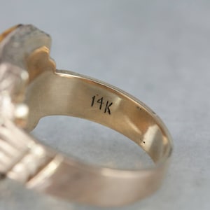 May include: A gold ring with a large, faceted tiger's eye stone set in a detailed, ornate setting. The ring is marked "14K" on the inside band.