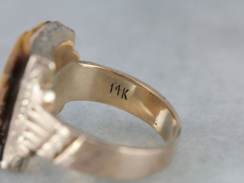 May include: A gold ring with a large, faceted tiger's eye stone set in a detailed, ornate setting. The ring is marked "14K" on the inside band.
