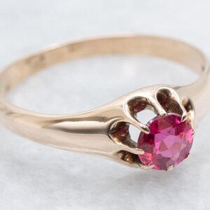 Op de afbeelding: Een gouden ring met een ronde, helder roze edelsteen. De edelsteen is gezet in een gedetailleerde, open zetting. De ring heeft een gladde, gepolijste band en een klassiek ontwerp.