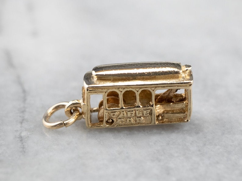 May include: Gold-toned charm shaped like a San Francisco cable car. The charm has the words "Cable Car" inscribed on the side.