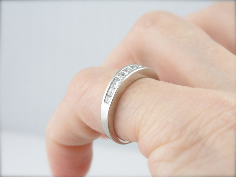 May include: A silver band with a row of small, square-shaped diamonds set in a channel setting.