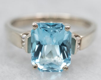 May include: A silver ring with a large, light blue aquamarine gemstone and smaller diamonds on the band.