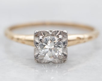 May include: A vintage engagement ring with a round brilliant cut diamond set in a square platinum setting. The band is yellow gold with a delicate engraved design.