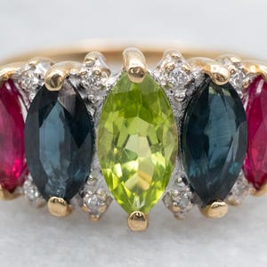 Pode incluir: Um anel de ouro com cinco pedras preciosas em forma de marquesa. As pedras são vermelhas, azuis, verdes, azuis e vermelhas. O anel é adornado com pequenos diamantes.