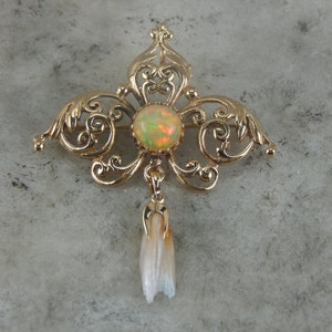 Può includere: Un broche in filigrana d'oro con una pietra di opale rotonda e una perla pendente.