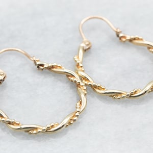 May include: A pair of gold hoop earrings with a twisted design and small beads along the edge.