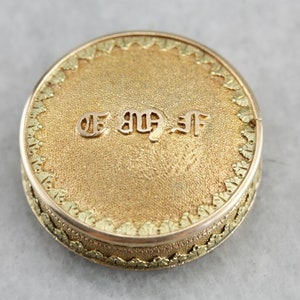 Puede incluir: Una caja redonda de color dorado para guardar joyas con un borde decorativo y la inscripción "E.M.F." en letras en relieve.
