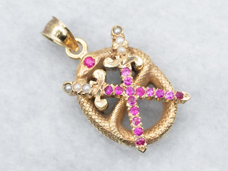 May include: Gold pendant with a snake design and two crossed swords set with pink and white stones.