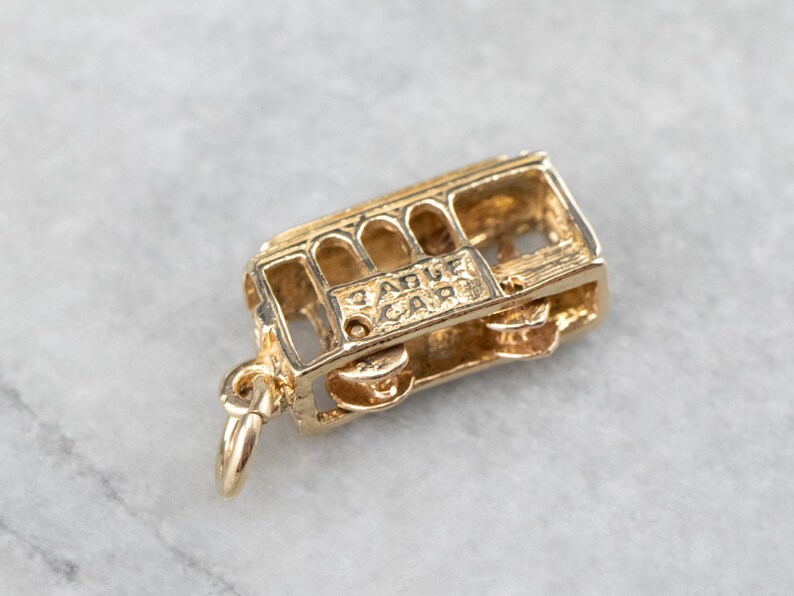 May include: Gold-toned charm in the shape of a San Francisco cable car. The charm has a detailed design and the words "Cable Car" are inscribed on the side.