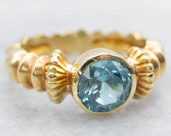 May include: A gold ring featuring a blue gemstone set in a bezel setting. The band is textured with a series of small, raised bumps.