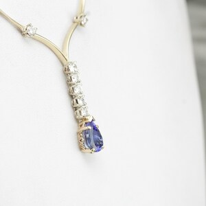 K&ouml;nnte beinhalten: Eine goldene Halskette mit einem birnenf&ouml;rmigen blauen Edelstein-Anh&auml;nger, der von kleinen Diamanten umgeben ist.