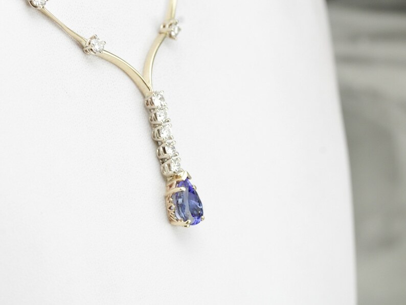 K&ouml;nnte beinhalten: Eine goldene Halskette mit einem birnenf&ouml;rmigen blauen Edelstein-Anh&auml;nger, der von kleinen Diamanten umgeben ist.