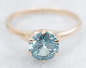 May include: A gold ring with a round, light blue gemstone set in a four-prong setting.
